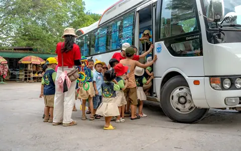 Niños subiendo a un bus acompañados por una adulta