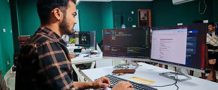 Desarrollador escribiendo código en una oficina con dos monitores